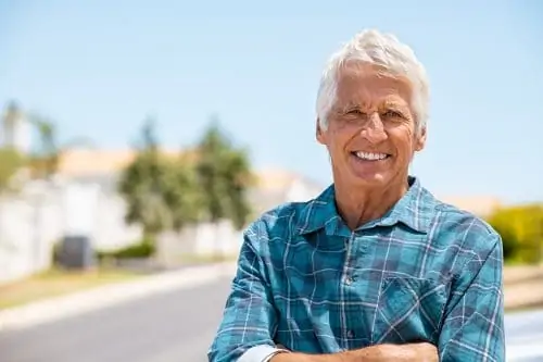 Retired old man standing outdoor with folded arms smiling and looking at camera. Successful mature man relaxing outdoor with copy space. Portrait of happy senior grandfather with crossed arms and big grin on face.