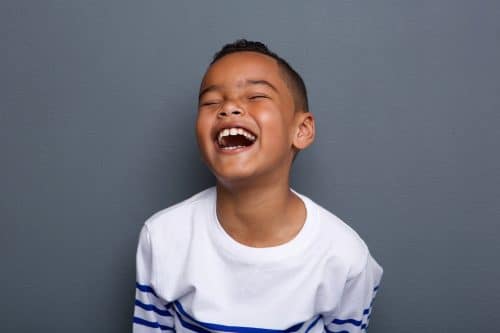 Close up portrait of an excited little boy laughing on gray background